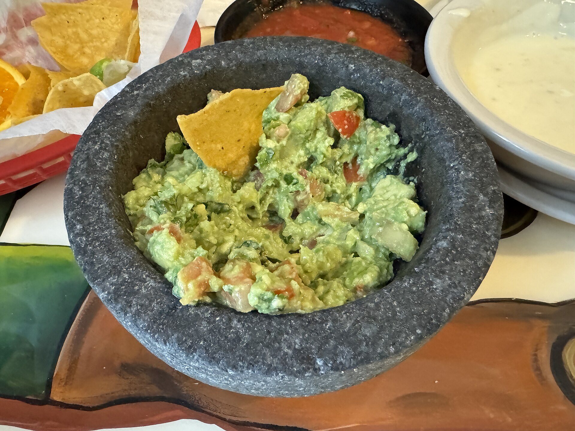 Chunky guacamole with tomato in a stone molcajete with a tortilla chip
