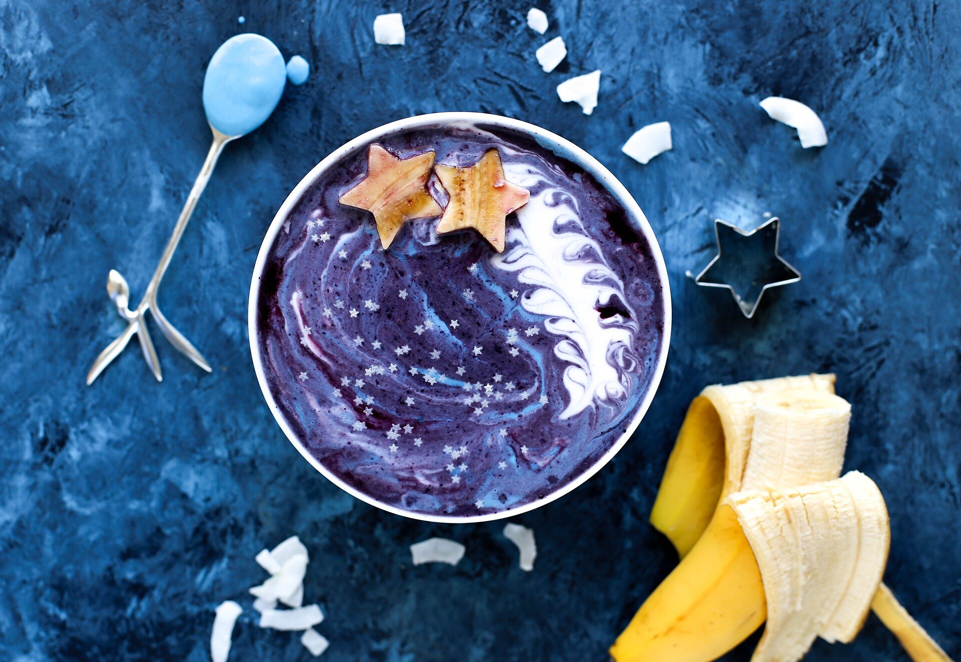 Purple berry smoothie bowl topped with coconut flakes and star-shaped fruit, with a banana on the side